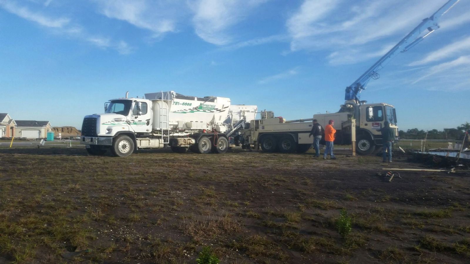 White Advantage Concrete mixer truck parked on a cleared lot, with a raised pump boom and a few workers behind it
